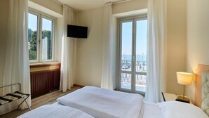 Quarto de hotel com duas camas, televisão, janela com vista e uma luminária.