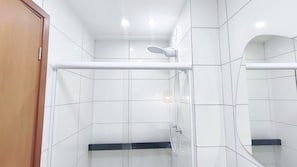Ein Badezimmer mit weißen Fliesen, einer Holztür, einer Duschkabine aus Glas und einem Spiegel.