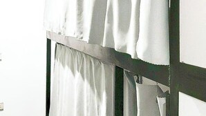 A room with a window covered by white curtains, a visible door frame, and a partial view of a wall.