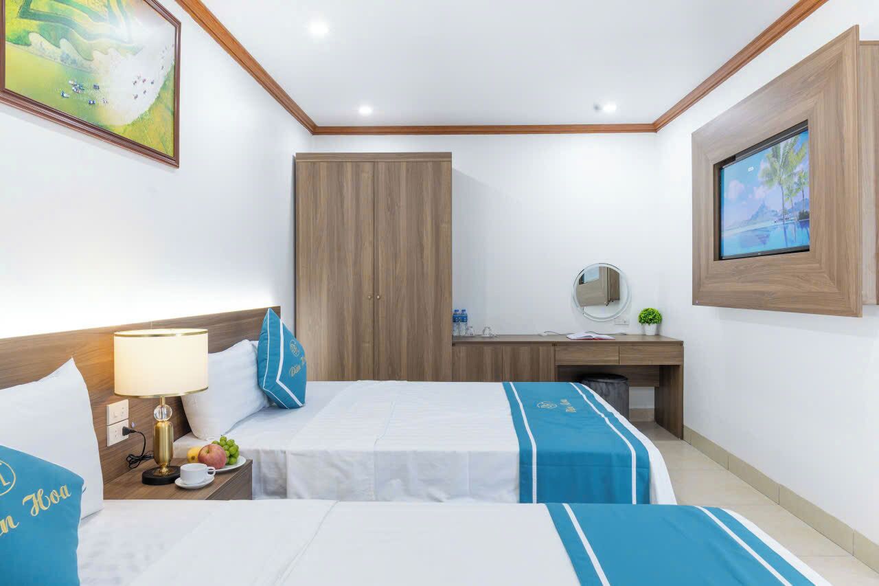 A hotel room with two beds, a desk, a wardrobe, a TV, and a painting on the wall.