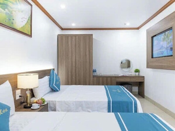 A hotel room with two beds, a desk, a chair, a nightstand, and a wall-mounted TV.