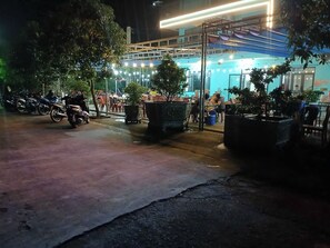 An outdoor seating area with tables and chairs, potted plants, and a motorcycle parked nearby.