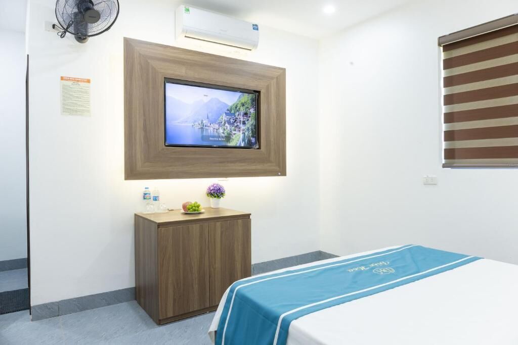 Une chambre d’hôtel avec un lit, un téléviseur fixé au mur, une petite armoire en bois et une fenêtre avec des stores.