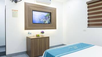 Une chambre d’hôtel avec un lit, un téléviseur fixé au mur, une petite armoire en bois et une fenêtre avec des stores.