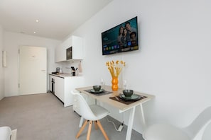 Eine moderne Küche mit weißen Schränken, einem flachbildfernseher über der Arbeitsplatte und einem Essbereich mit Tisch für zwei Personen.