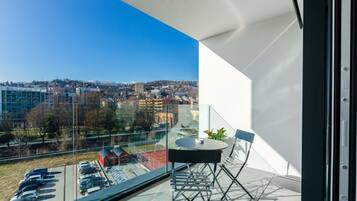 Ein Balkon mit Tisch und Stühlen, einer Glastrennwand und Blick auf eine Stadtlandschaft.