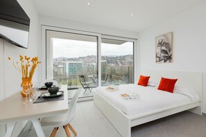 Ein modernes Hotelzimmer mit Bett, Essbereich und großem Fenster mit Blick auf die Stadt.