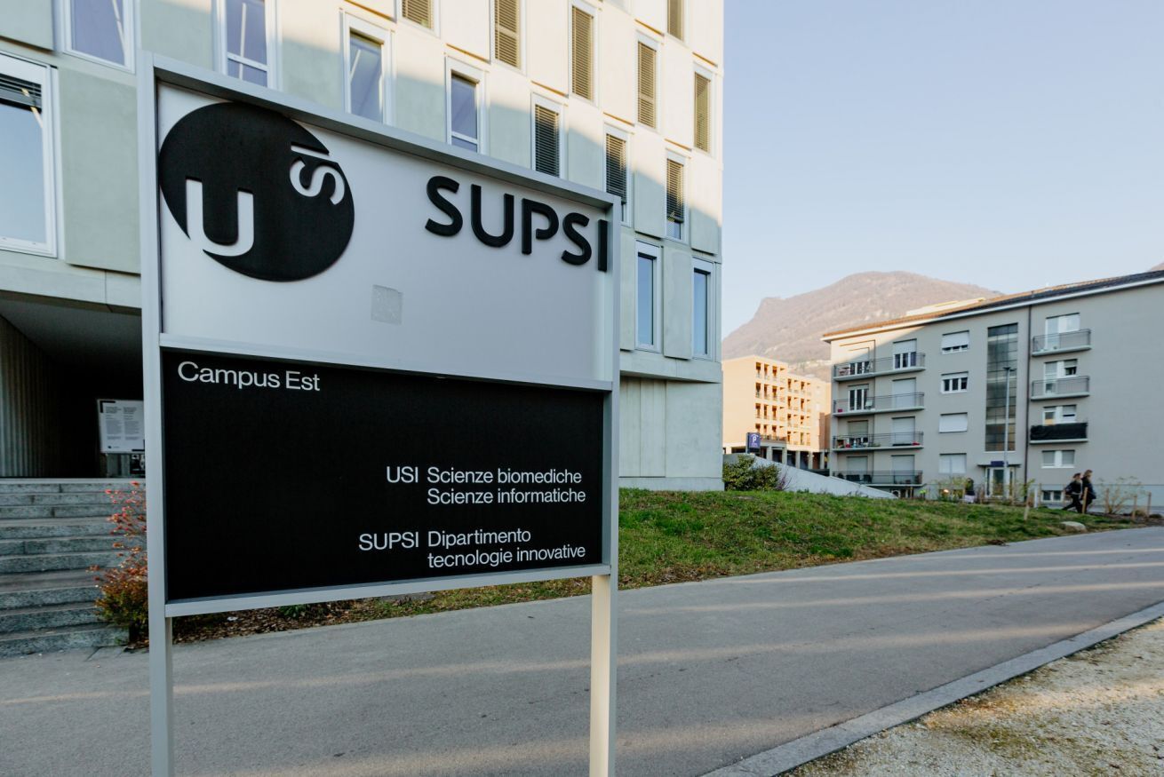 Ein Schild mit der Aufschrift 'SUPSI Campus Est', im Hintergrund ein modernes Gebäude.