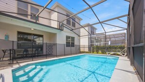 Piscina com cobertura de vidro, área de varanda coberta com cadeiras e um edifício com grandes janelas.