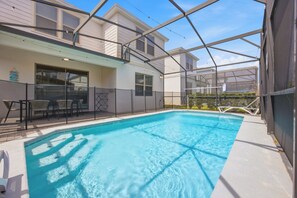 Ein Schwimmbad mit Glasveranda, eine überdachte Terrasse mit Sitzgelegenheiten und ein Gebäude mit großen Fenstern.