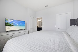 Ein Schlafzimmer mit einem großen Bett, einem Fernseher auf einer Kommode und einer Tür zu einem Badezimmer.