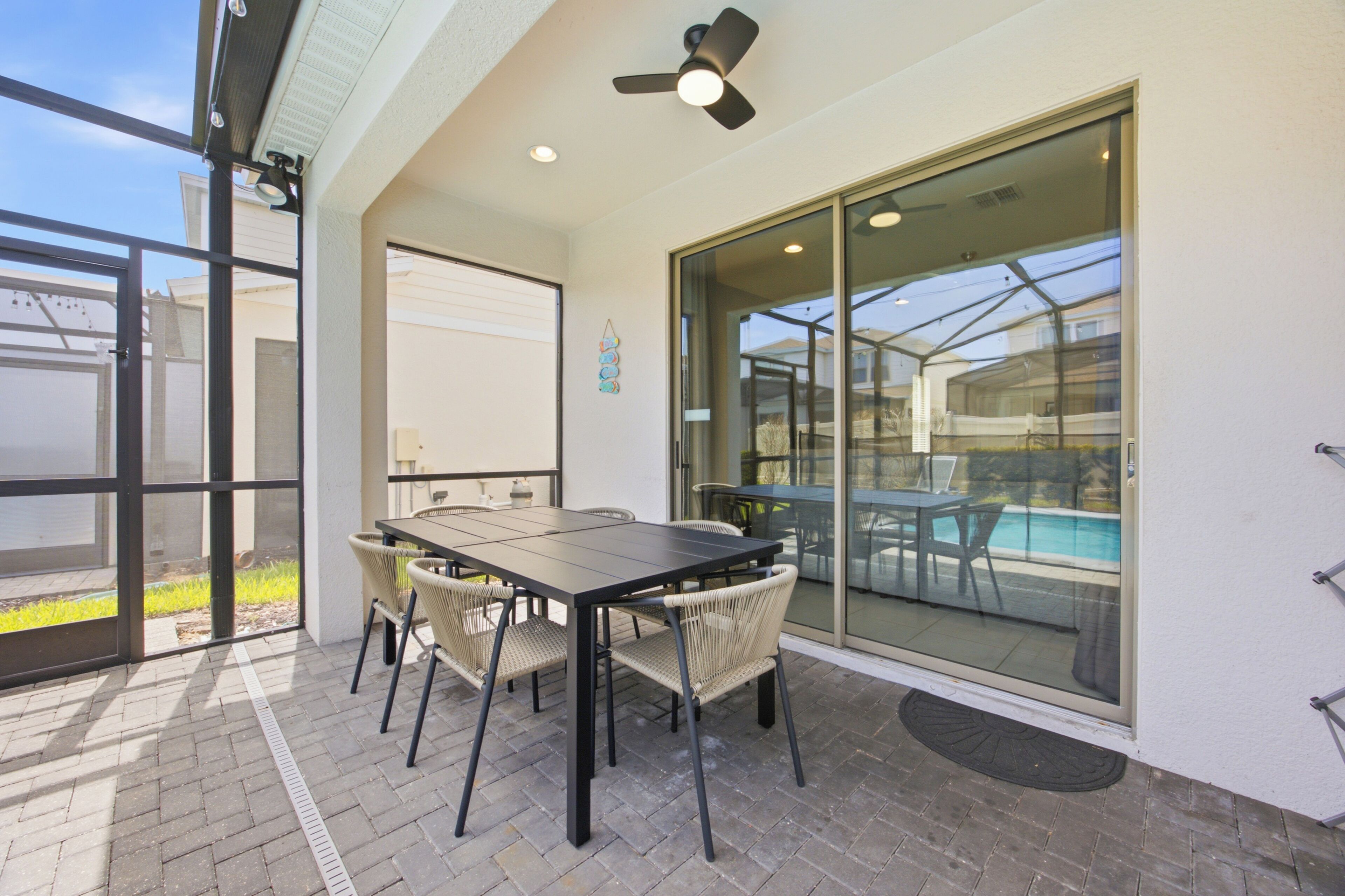 An outdoor patio with a table and chairs, a ceiling fan, and a glass door leading to a pool area.