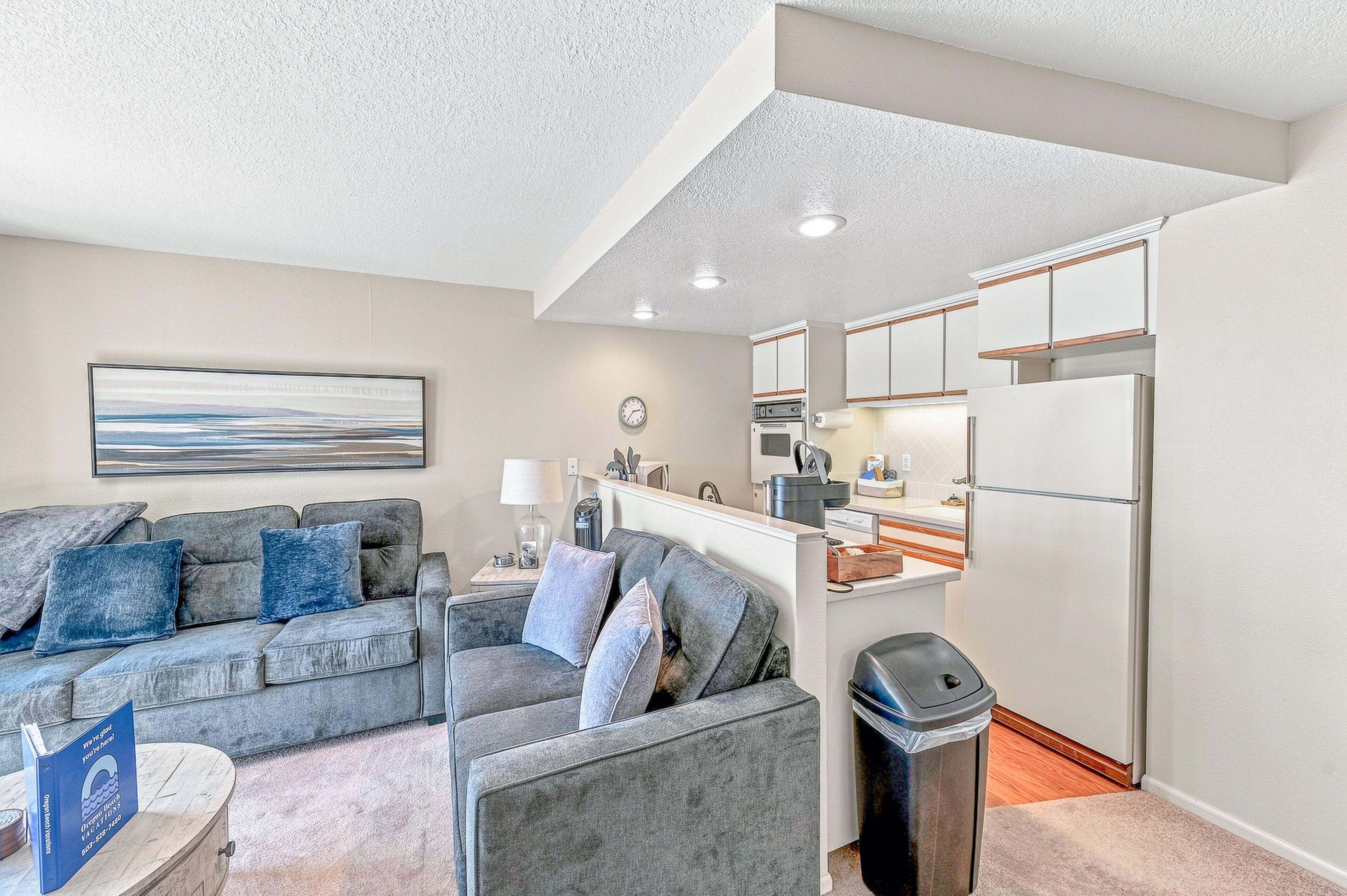 A modern living room with a grey sofa, a coffee table, and a trash bin.