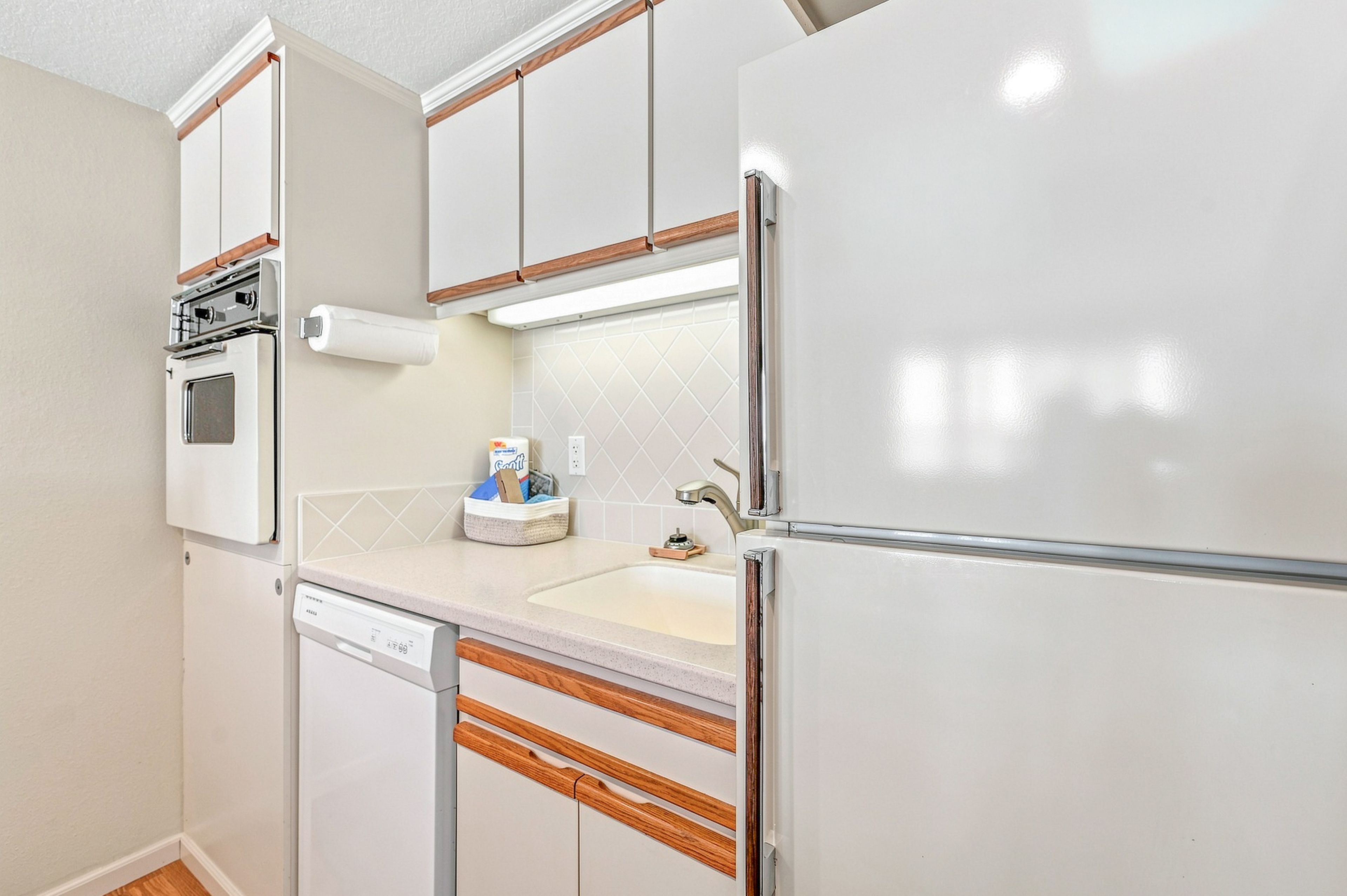 A compact kitchen with a built-in oven, a dishwasher, a refrigerator, and a countertop with a sink.