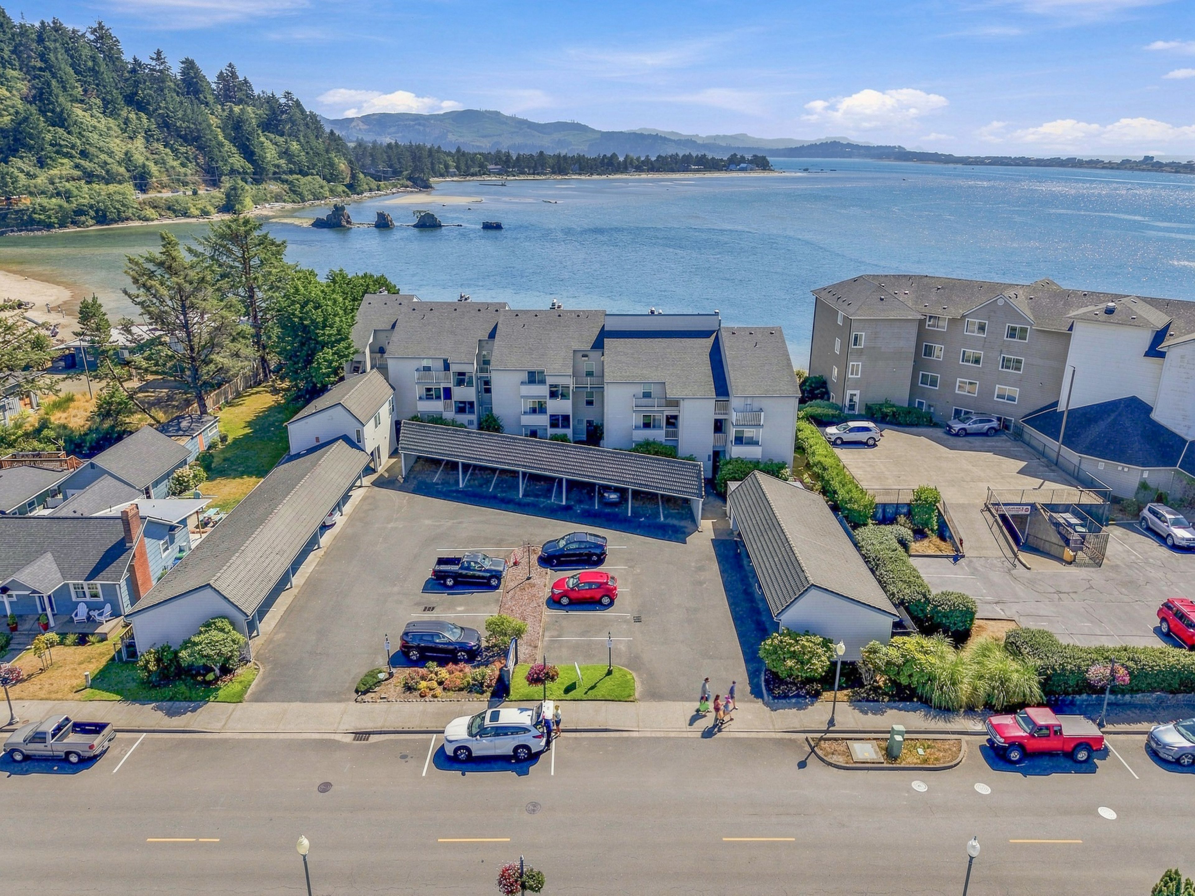 A multi-story hotel with a parking lot, adjacent to a body of water with boats.