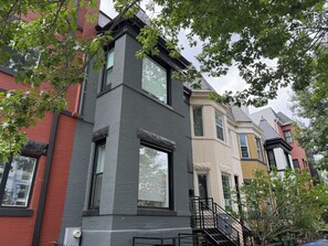 A row of townhouses with large windows, a visible front door, and a staircase leading to the entrance.
