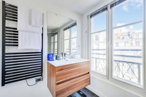 A bathroom with a wooden vanity, a large mirror, a towel rack, and a window with a view of buildings. - Charming Apartment a/c 1br/2p - Le Marais (Paris)