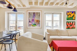 A modern living room with a dining area, large windows, a sofa, and a table with a red tablecloth. - Charming Apartment a/c 1br/2p - Le Marais (Paris)