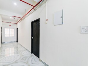 Ein Flur mit einer schwarzen Tür, einer weißen Wand mit Lichtschalter und einem gemusterten Boden.