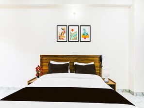 Ein ordentlich bezogenes Bett mit Holz-Kopfteil, ein Nachttisch mit Lampe und drei gerahmte Kunstwerke an der Wand.