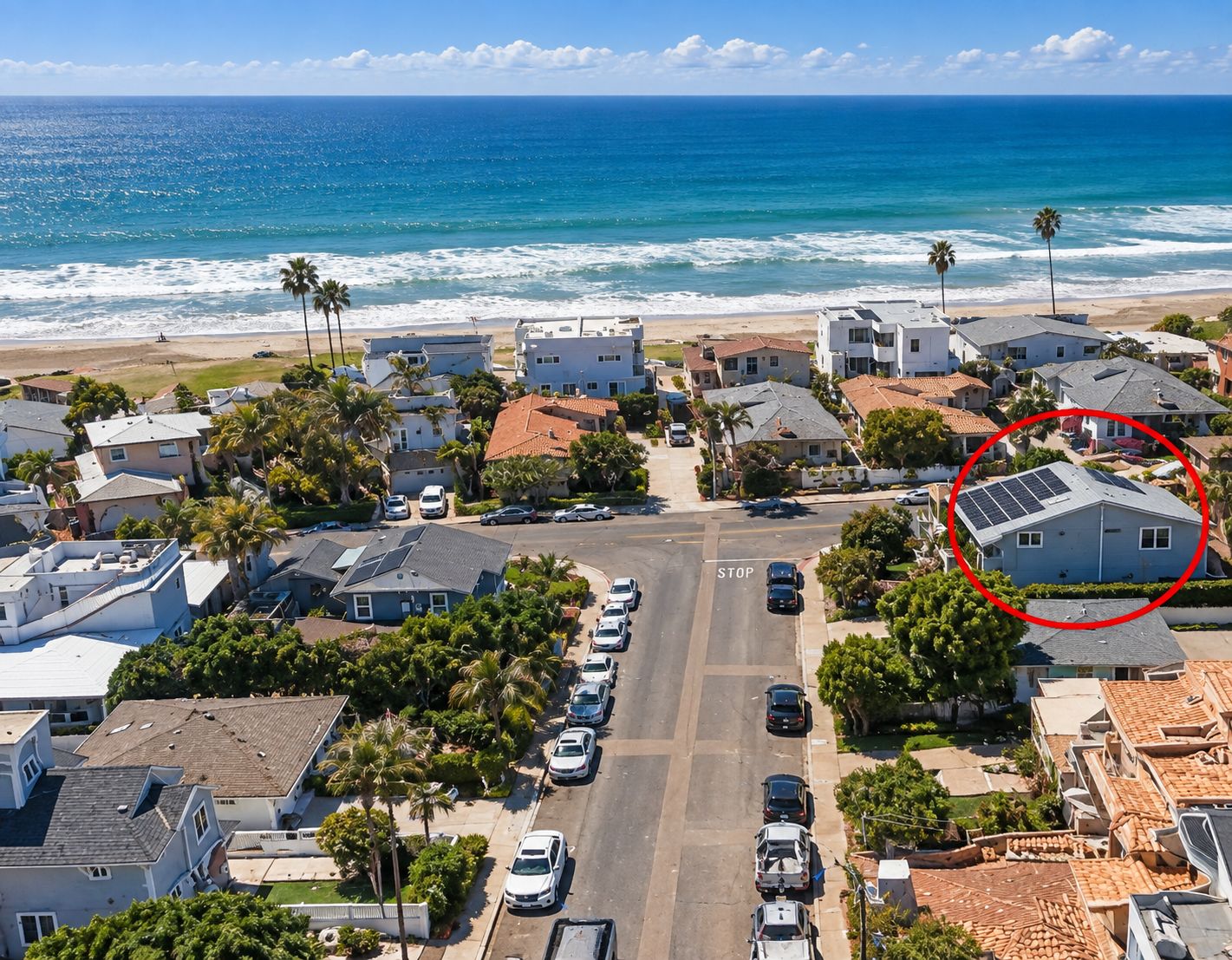 Un quartier résidentiel avec une rue menant à la plage, des maisons équipées de panneaux solaires et un panneau de signalisation indiquant un stop.