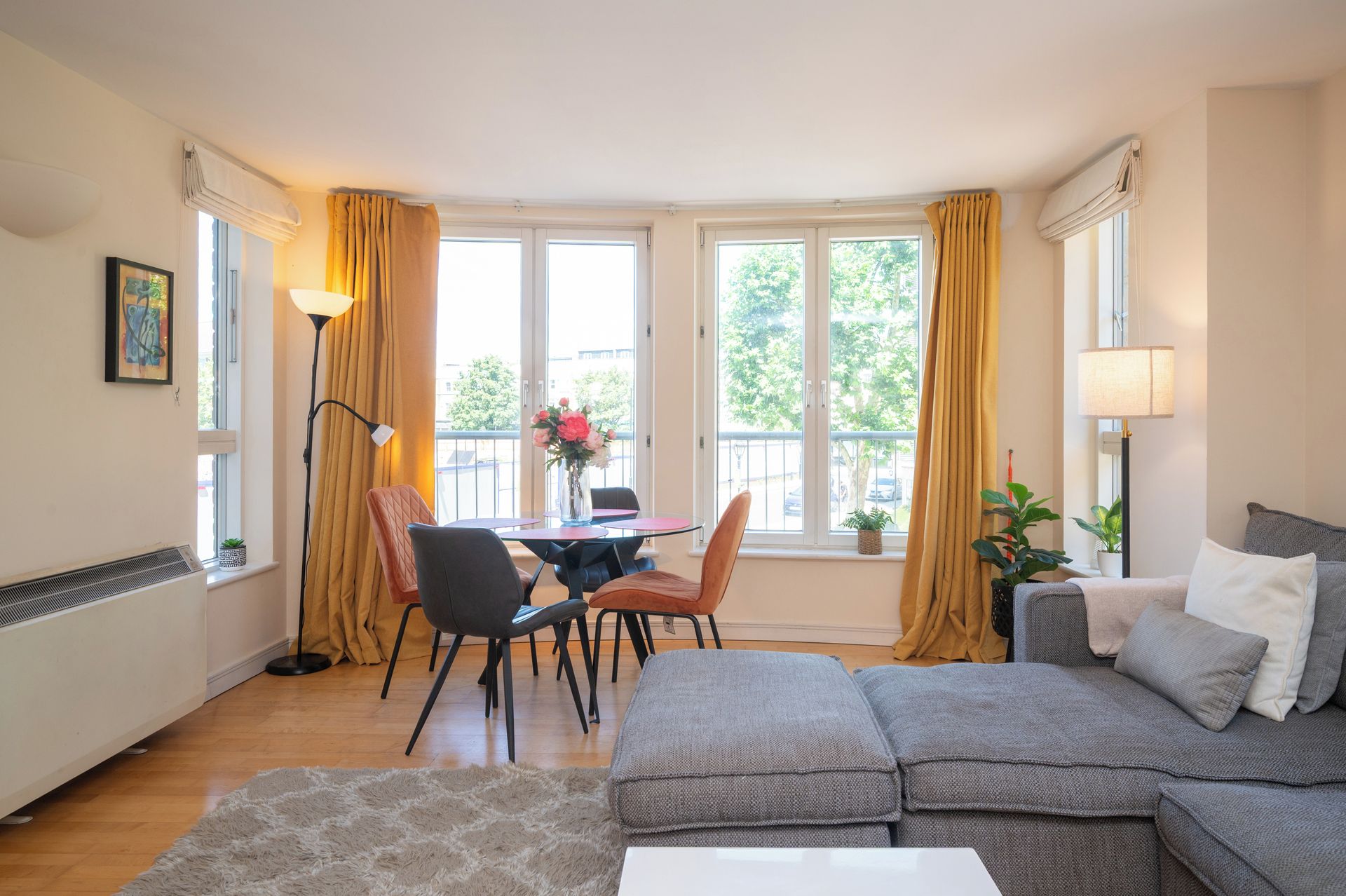Un salon moderne avec un canapé, une table à manger et des chaises, ainsi qu’une grande fenêtre avec des rideaux.