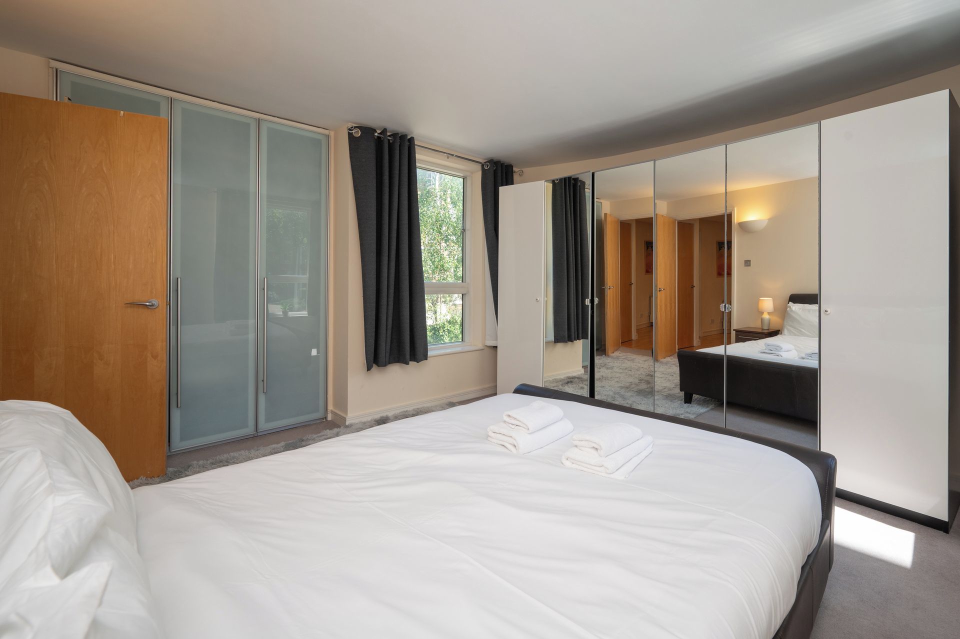 A hotel room with a large bed, a wardrobe, a mirror, and a view of another room.