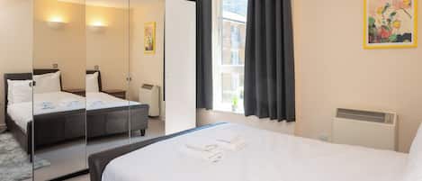 Une chambre d’hôtel avec deux lits, un grand miroir, une fenêtre avec des rideaux et un radiateur.