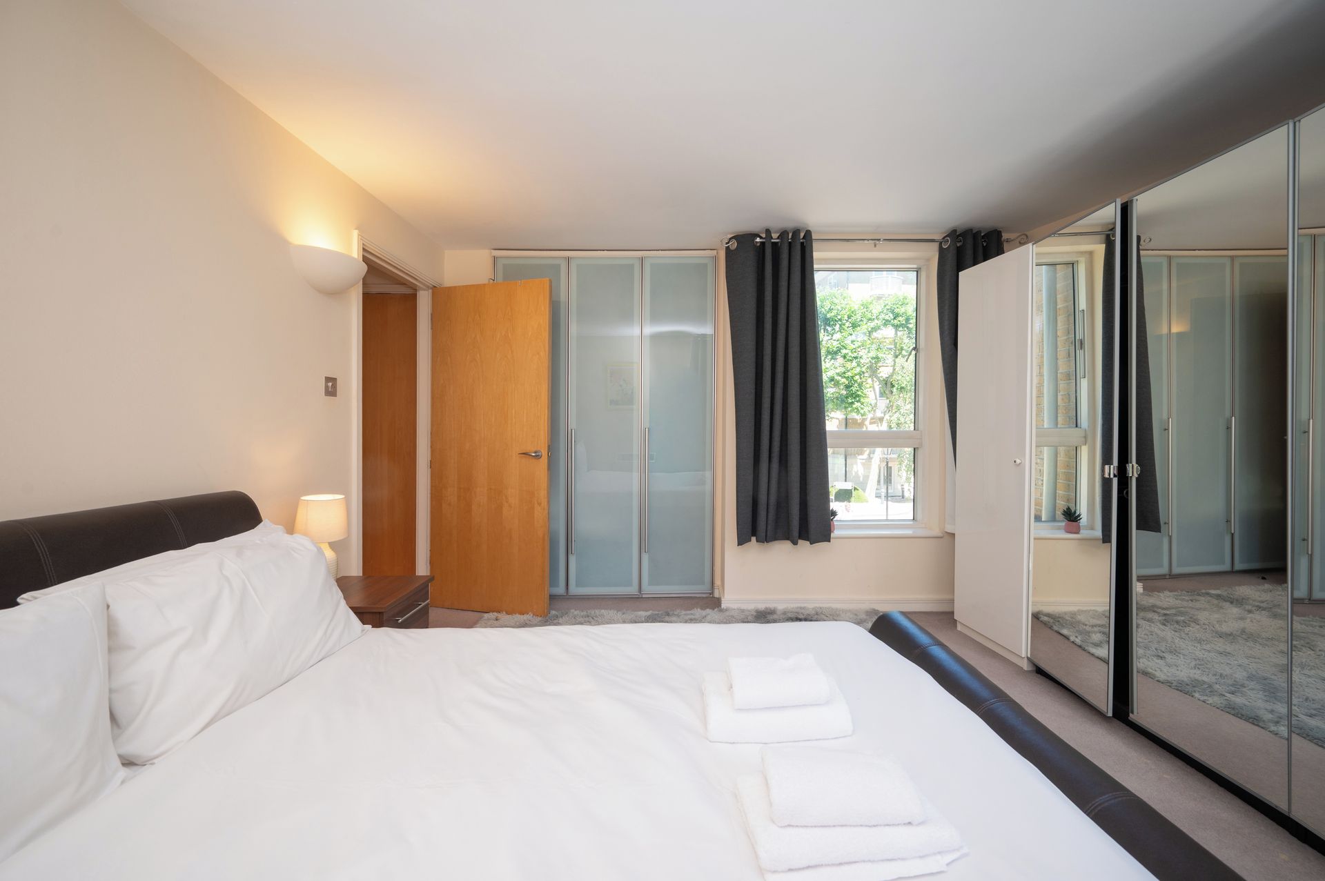 Een hotelkamer met een bed, een kledingkast, een spiegel en een raam met gordijnen.