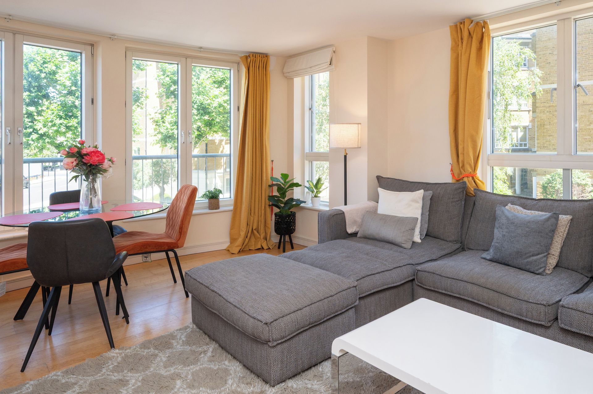 Un salon moderne avec un canapé d’angle gris, une table basse blanche et un coin repas comprenant une table et des chaises rouges.