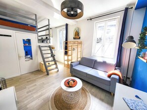 A compact living space with a loft bed, a sofa, a coffee table, and a large window providing natural light. - Le Cocon: A Cozy Haven in the Heart of Rouen (Rouen)