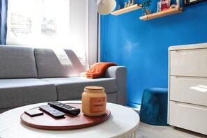 Ein Wohnzimmer mit einer Couch, einem Couchtisch mit Fernbedienungen, einer Honigglas und einer blauen Wand.