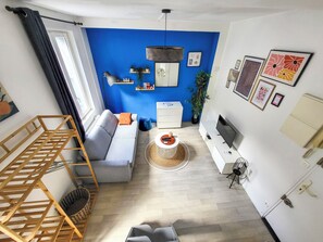 Ett modernt vardagsrum med en blå accentvägg, en grå soffa, en trähylla, en tv och ett soffbord.