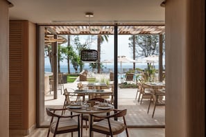 Un espace repas avec des tables et des chaises, une pergola et une vue sur la piscine et l’océan.