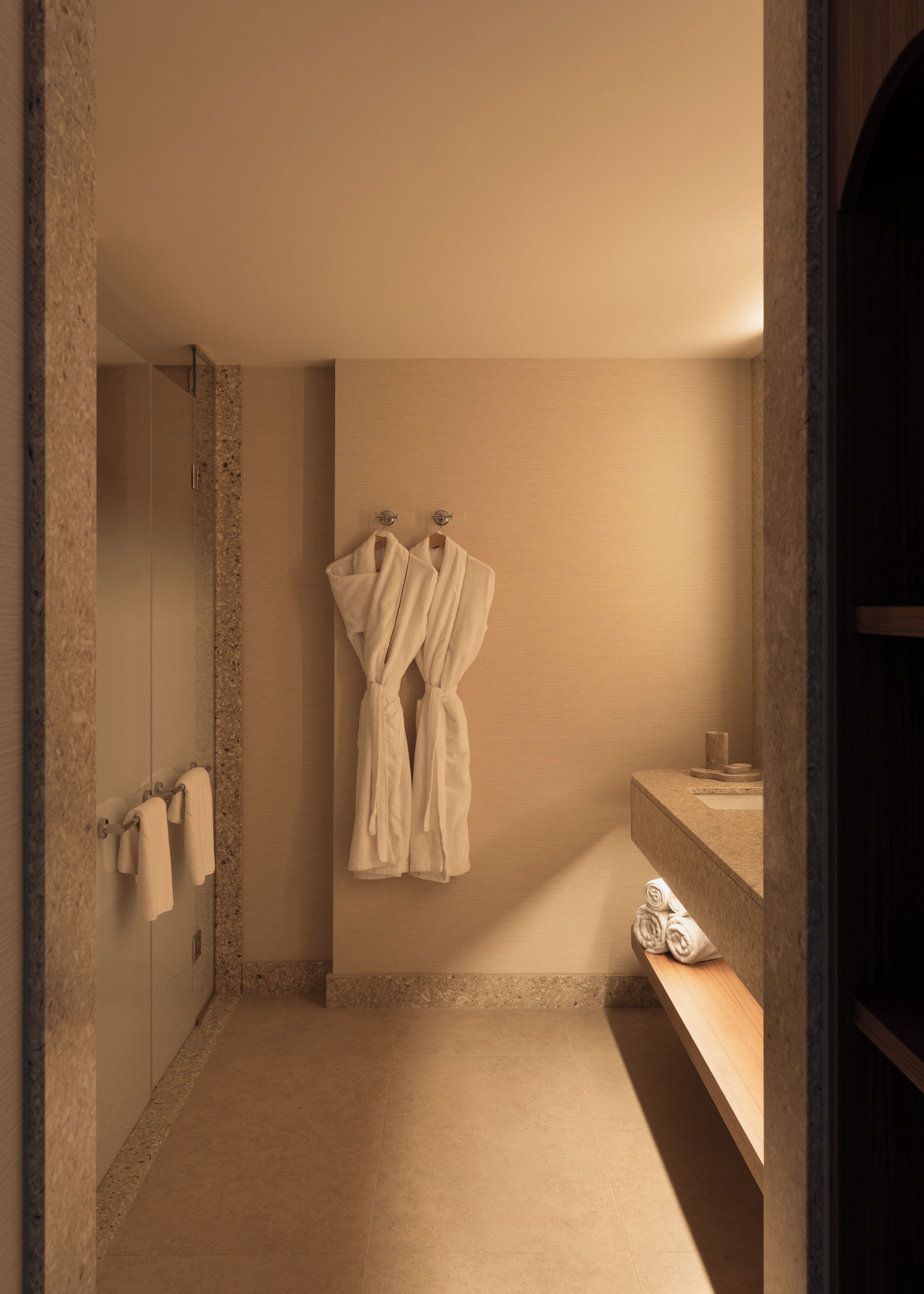 A bathroom with a shower, a towel rack with towels, and a wooden vanity.