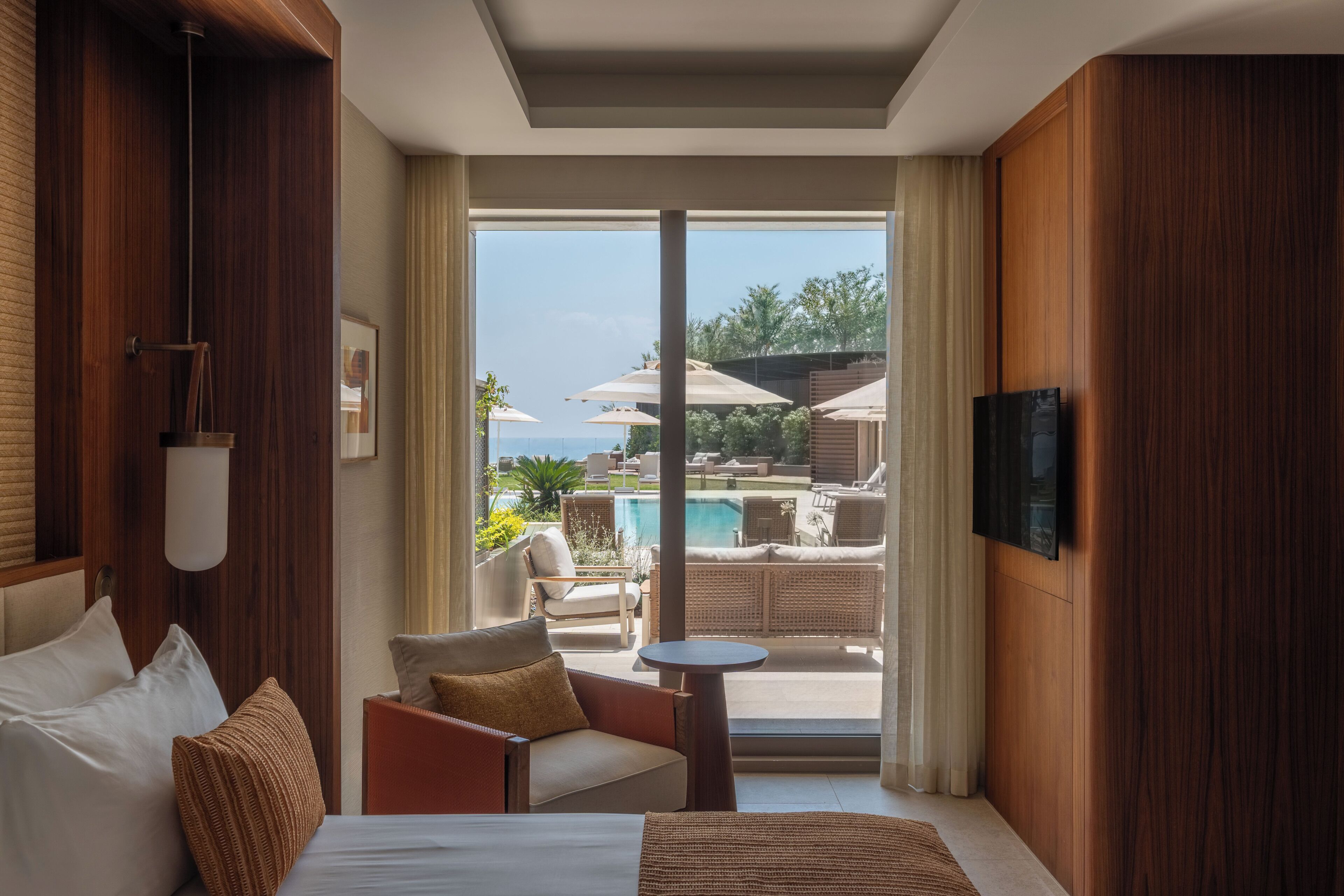 Una camera d'albergo con un letto, una sedia, un tavolino, una TV e vista su una piscina all'aperto.