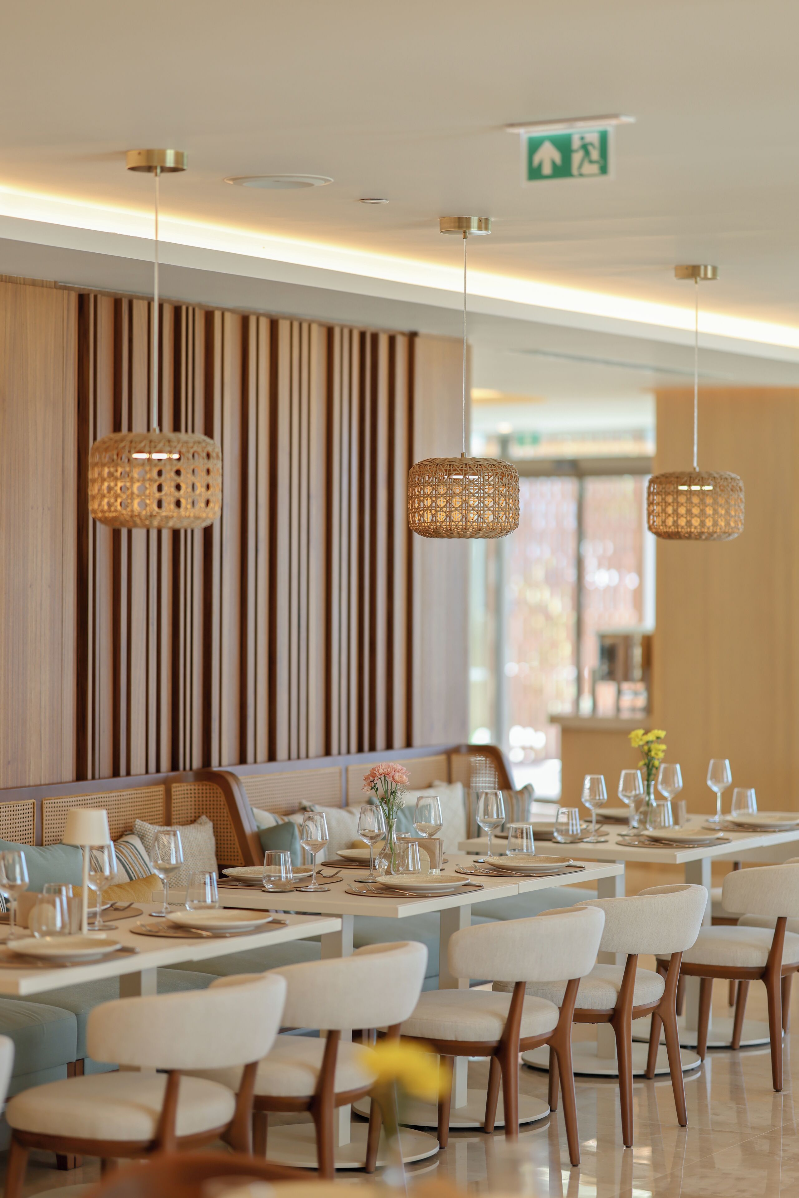 Un comedor moderno con mesas largas, sillas y lámparas de mimbre colgantes.