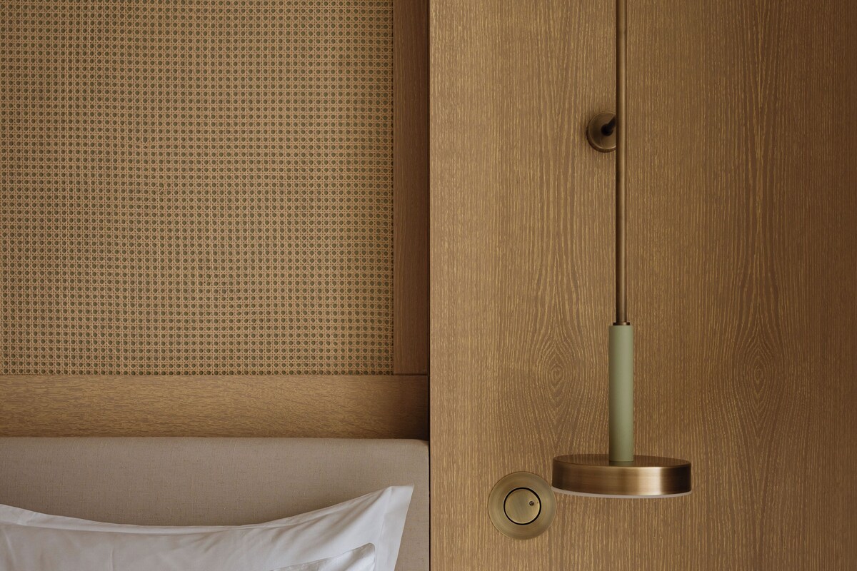 Una cama con sábanas blancas, almohada verde, cabecera de madera con diseño tejido y una puerta con tirador de latón.