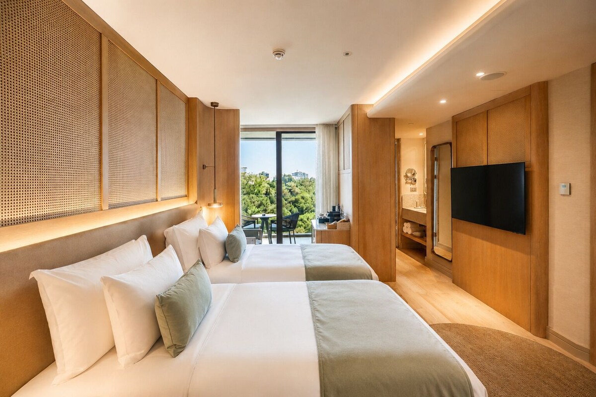 Habitación de hotel con dos camas, televisión, balcón con vistas y zona de comedor.
