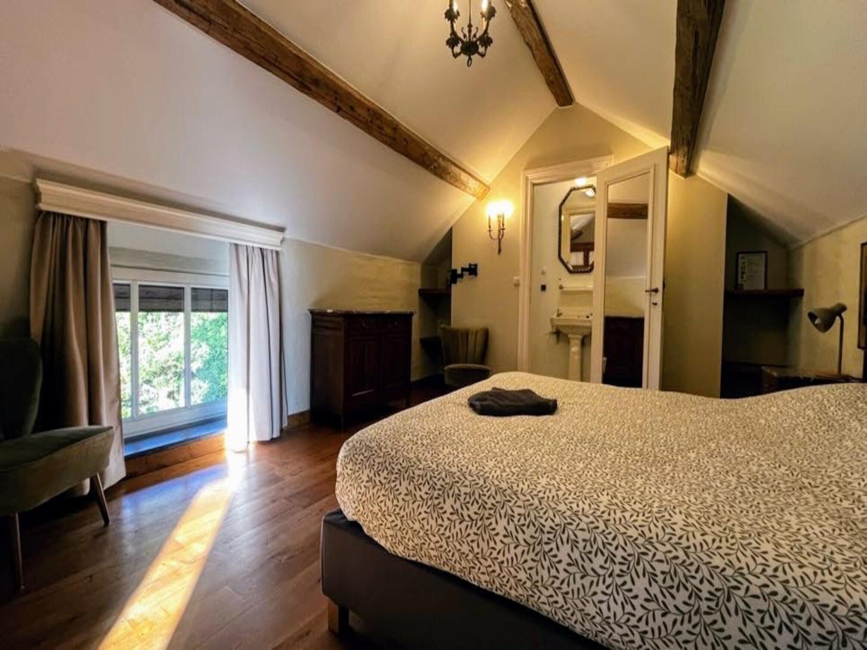 A bedroom with a large bed, a window with curtains, a wooden ceiling, and a nightstand.