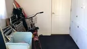 En smal hall med ett cykelställ, en dörr och en blå stol.