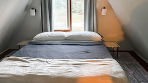 Ein Schlafzimmer mit einem Bett, zwei Nachttischen, einem Fenster mit Vorhängen und einer Wandlampe.