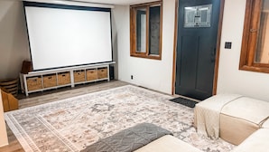 Ein Wohnzimmer mit großem Bildschirm, einer Tür, einem gemusterten Teppich und einem Sofa.