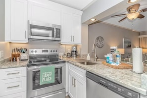 A kitchen with white cabinets, stainless steel appliances, a clock, and a ceiling fan. - Ocean Creek Resort: 7-min walk to beach (Myrtle Beach)