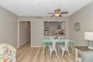 A dining area with a glass table and chairs, a ceiling fan, and a kitchen in the background. - Ocean Creek Resort: 7-min walk to beach (Myrtle Beach)