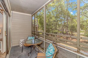 A covered porch with wicker furniture, a glass table, and a view of a wooded area. - Ocean Creek Resort: 7-min walk to beach (Myrtle Beach)
