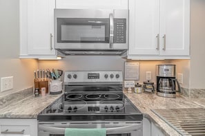 A kitchen with white cabinets, a stainless steel stove, a microwave, and a coffee maker. - Ocean Creek Resort: 7-min walk to beach (Myrtle Beach)