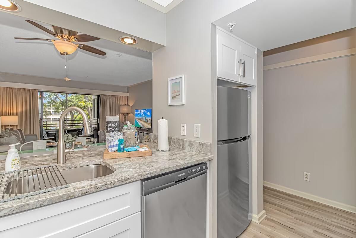 A modern kitchen with a built-in dishwasher, stainless steel refrigerator, and a ceiling fan.