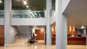Eine moderne Hotelhalle mit einer Rezeption, einer Treppe und einem Balkon im zweiten Stock.