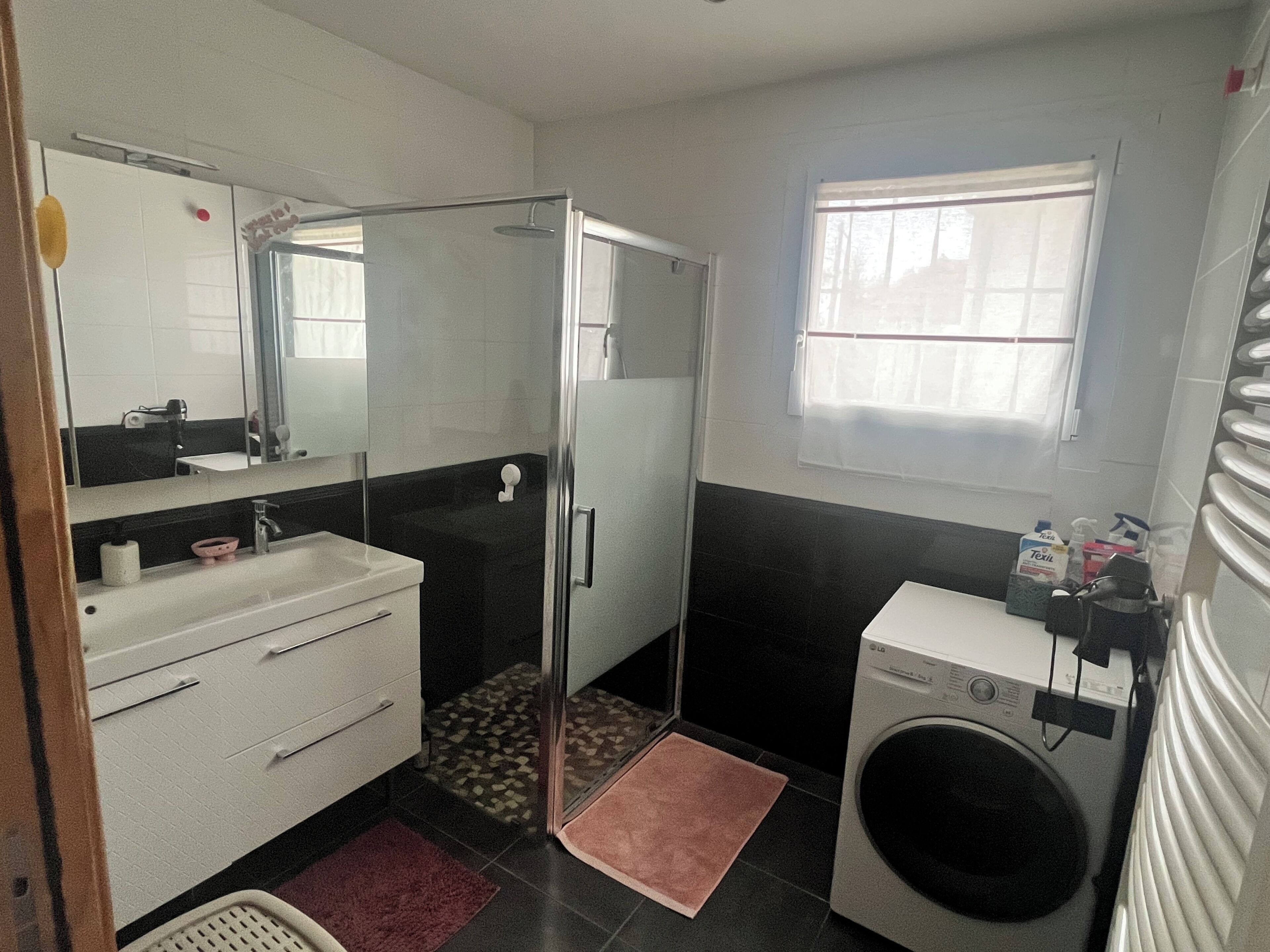 A bathroom with a shower, sink, mirror, and a window.